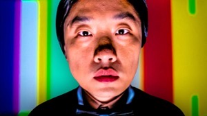 Jimmy O. Yang looking straight into the camera with a colorful background behind him