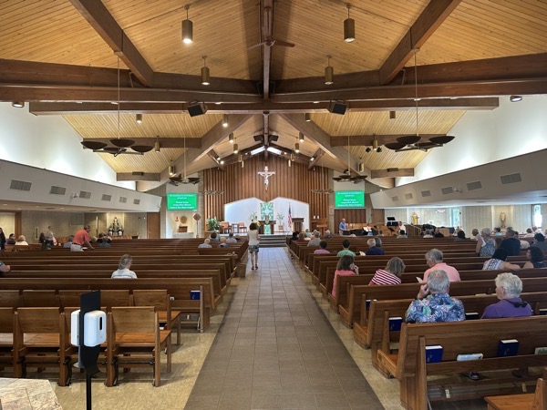 The view of the sanctuary from the back of the church, A pair of flat-screen TVs serve to provide lyrics for songs. There are decorative balconies on either side of the church (the roof is too los to allow these to be habitable and the church is clearly post-Vatican II in its design.