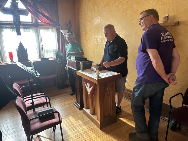 The altar in the chapel, a small wooden structure. Before it is a music stand holding a speaker adn tablet for those participating in the Mass via streaming.