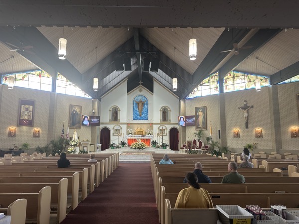 A view of the sanctuary of the church. A statue of the resurrected Christ is positioned over the tabernacle where traditionally a crucifix would appear. There is a crucifix to the left of the sanctuary. The clerestory stained glass windows are relatively recently installed
