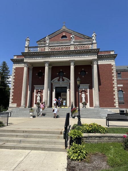 The view of the front of the chapel stairs leading up to a red brick and granite structure with statues of saints above the portico.