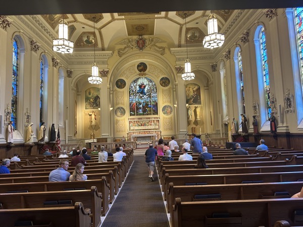 A view of the sanctuary from the back of the church. The church features a ceiling with numerous frescos and on the wall above the altar is a stained glass window depicting the Assumption of Mary