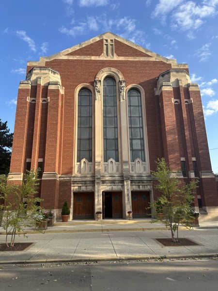 THe front of the church, a massive brick and granite façade with tall stained glass windows over the entrances,