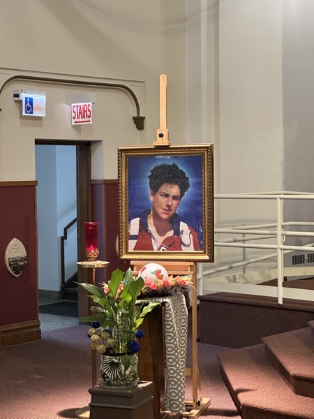 A photo of Carlo Acutis which was on display at the front of the church. In front of the photo is a basket with a soccer ball and iPad that were brought into the church during the opening procession. The altar boy who brought the soccer ball in couldn’t resist tossing it in the air (just a few inches) as he carried it). 