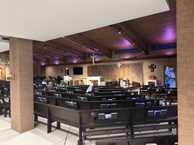 A view of the inside of the church showing the sanctuary and the pews arranged in a semicircle 6 pews deep, which is small for a church of this style