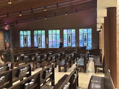 The view of the street side of the church showing a wall of clear glass windows only partly obscured with stained glass images of the four evangelists