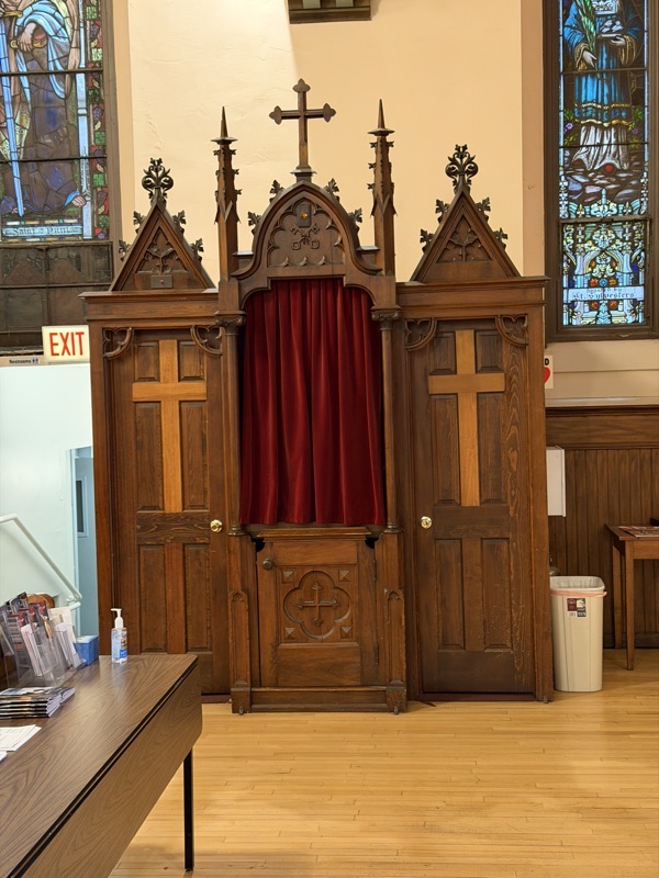 IMG_1200.jpeg An original confessional. The priest woudl be seated in the center behind the red curtain and on either side are enclosed booths for the penitents to give their confession. It’s made of stained wood with yellow crosses on the doors to the booths.