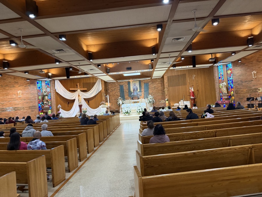 A view of the sanctuary from the back of the church. The walls are mostly brick, but there is wood panelling on the sides of the rear of the sanctuary. A banner behind the altar depicts Jesus as the Good Shepherd with the image somewhat inexplicably labeled in German (the neighborhood, before it was Latino was predominantly Czech and Polish).